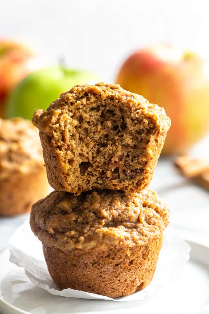 Two healthy apple muffins stacked, one with a bite taken out of it.