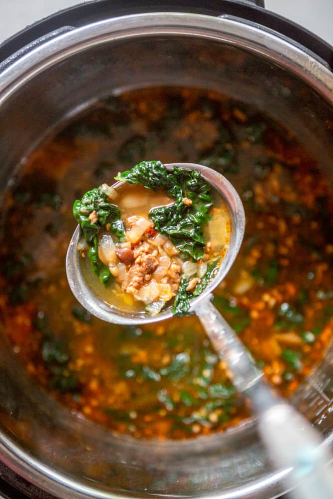 A ladle filled with sausage bean and kale soup over an instant pot filled with soup.
