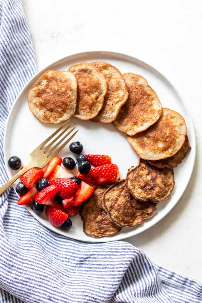 A plate of two ingredient banana pancakes with a side of strawberries and blueberries