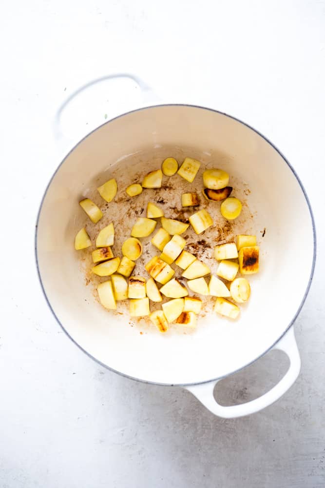 Diced parsnips being cooked in a white dutch oven.