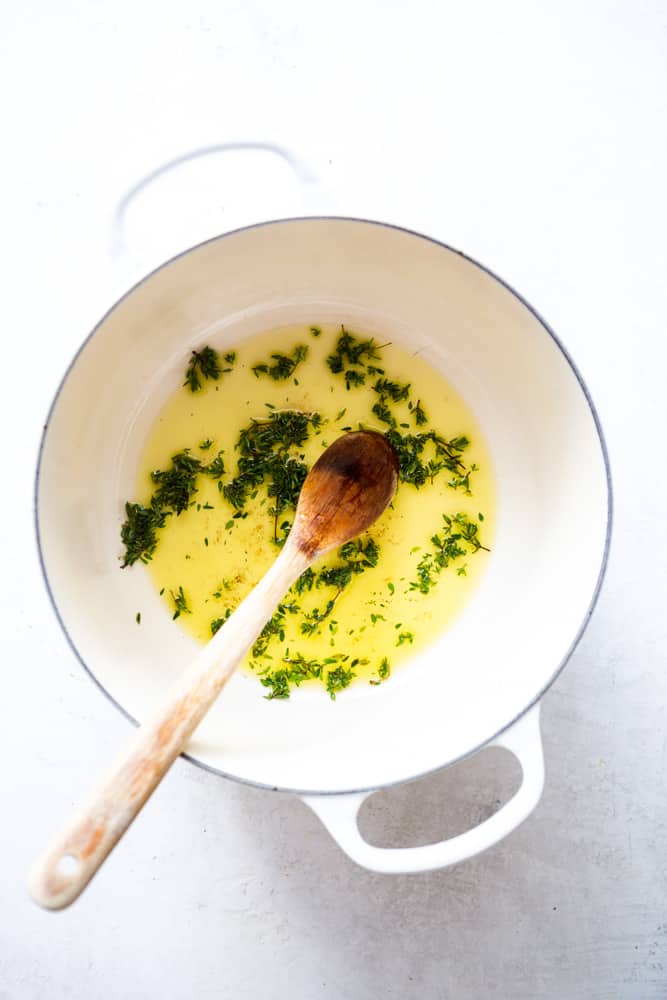 Olive oil and fresh thyme in a white Dutch oven