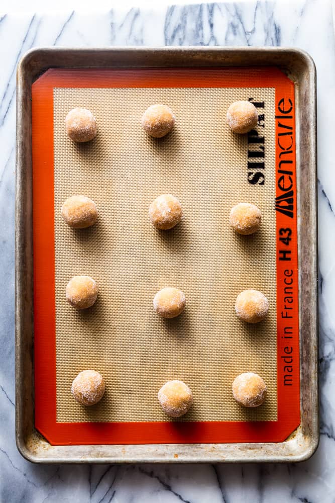 Peanut butter cookie dough balls on a cookie sheet lined with Silpat