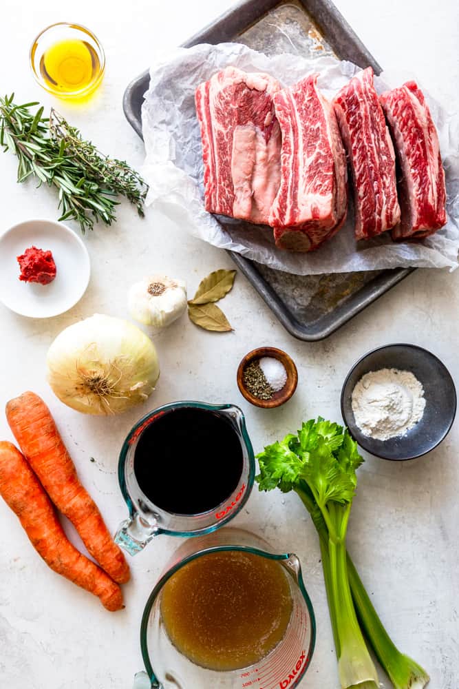 Ingredients for red wine braised short ribs - olive oil, herbs, tomato paste, garlic, bay leaves, onions, carrots, red wine, salt and pepper, celery, beef broth, flour, and short ribs.