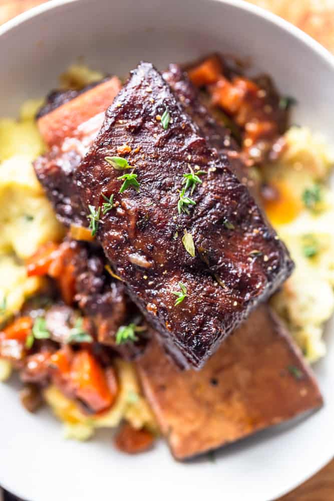 Close up of a browned red wine braised short rib garnished with fresh thyme, on top of a bed of mashed potatoes.