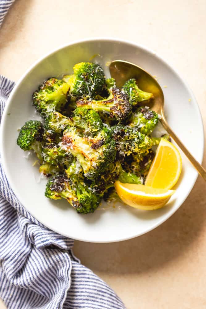 A white bowl of roasted broccoli garnished with parmesan cheese and lemon zest.