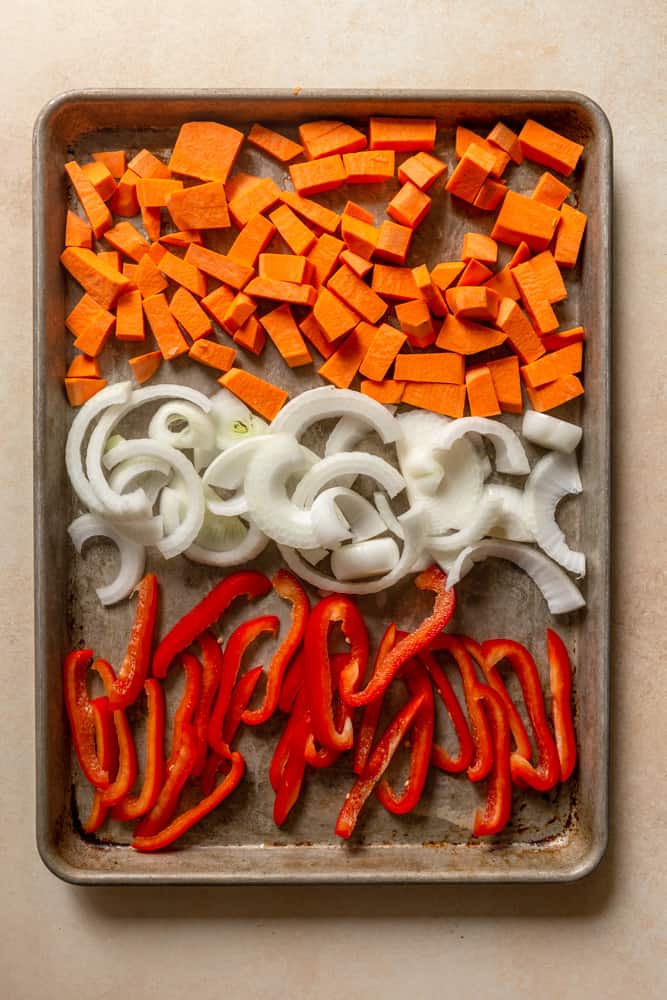 Cubed sweet potatoes, sliced sweet onion and sliced red bell pepper on a sheet pan.