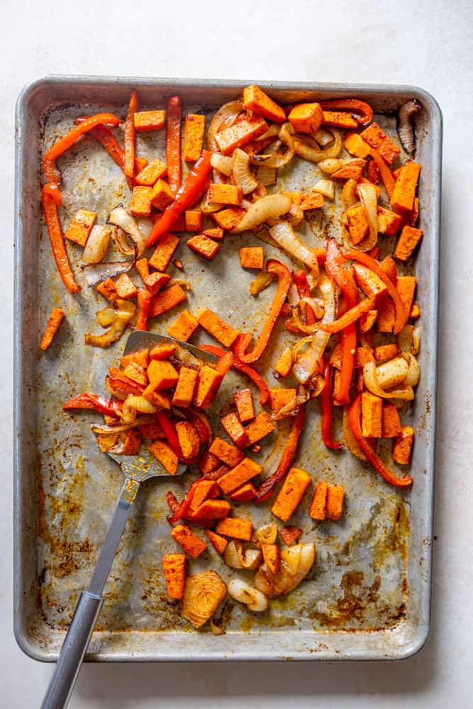 Roasted sweet potato, red bell pepper and onion on a sheet pan.
