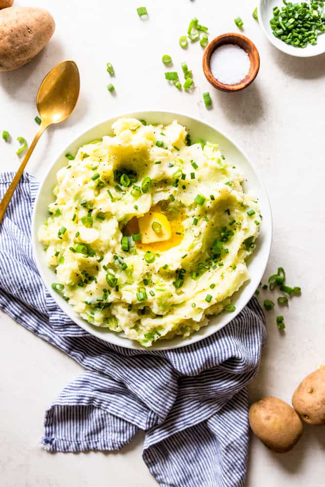 A bowl of colcannon garnished with sliced green onions and a large pool of butter.