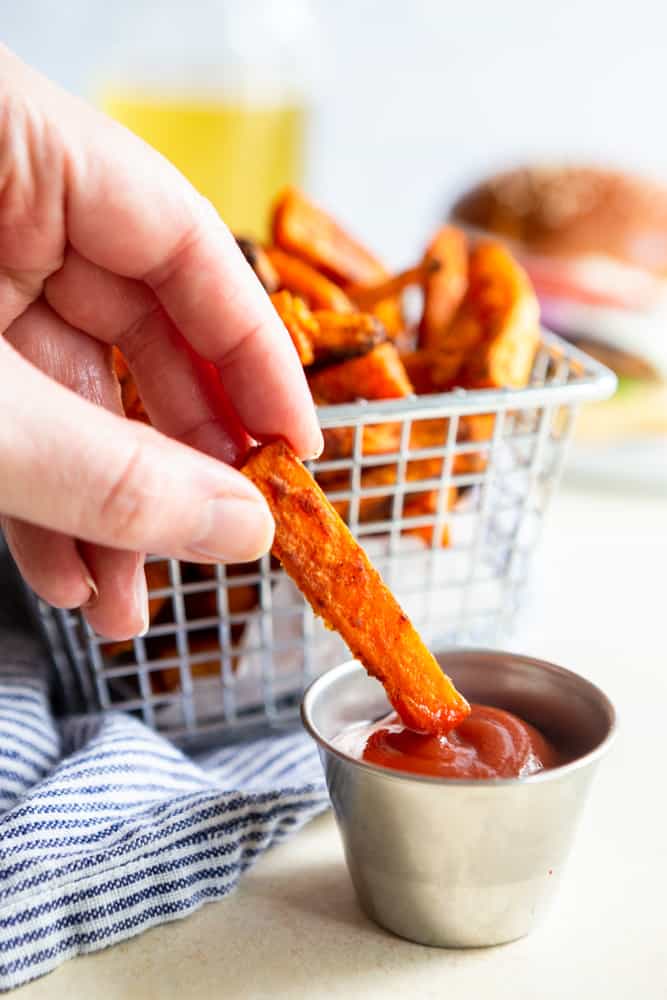 A sweet potato fry being dipped into ketcup.