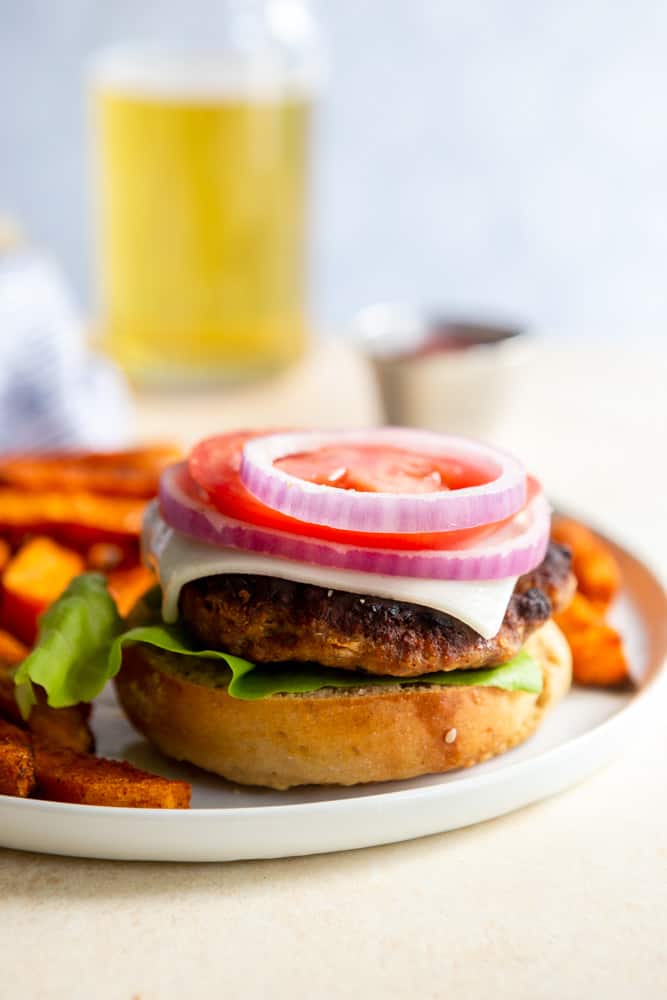 A turkey burger on half of a bun with lettuce, cheese onion and tomato.