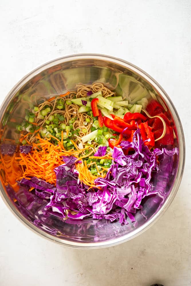 Chopped purple cabbage, grated carrots, sliced green onion, sliced cucumber and sliced re bell pepper in a large bowl with cooked spaghetti