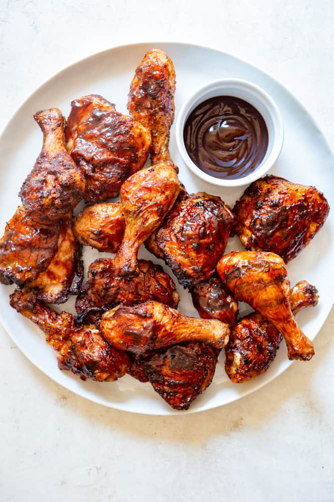Large white platter with grilled BBQ  chicken thighs and drumsticks.