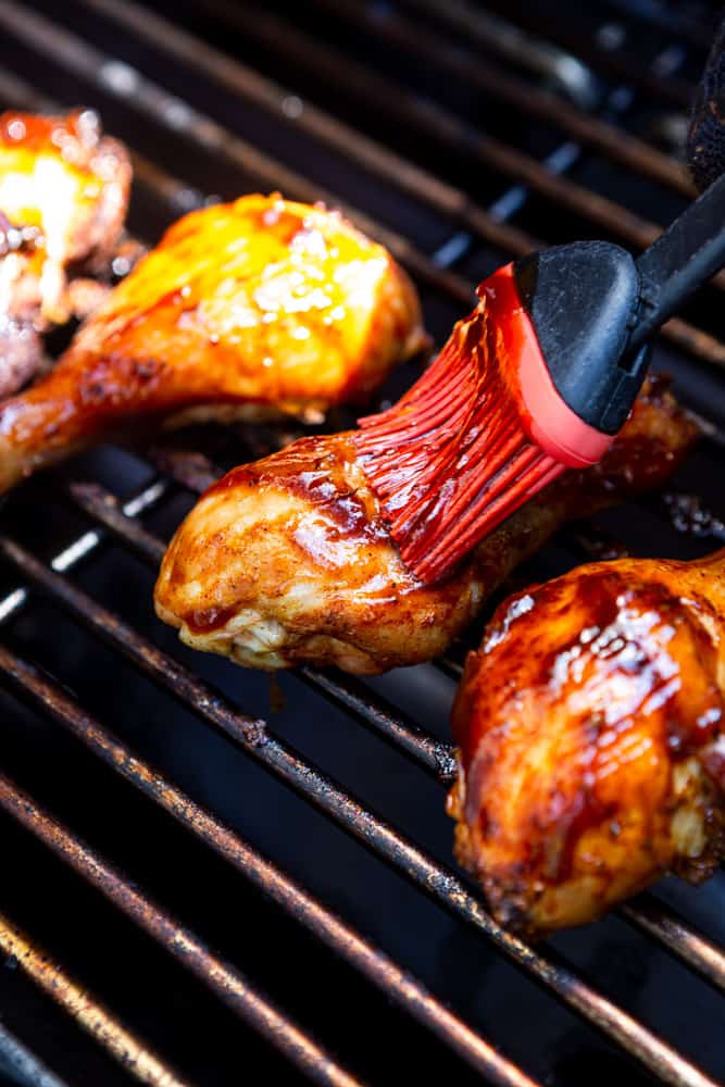 Chicken drumsticks on a grill, being brushed with BBQ sauce