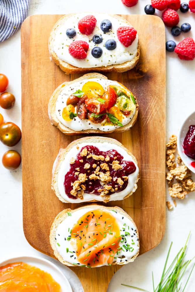 Several varieties of whipped cottage cheese toast on a wooden Board
1. blueberries, raspberries and hemp hearts
2 tomatoes bruschetta
3. jam and granola
4. smoked salmon, chives and black sesame seeds