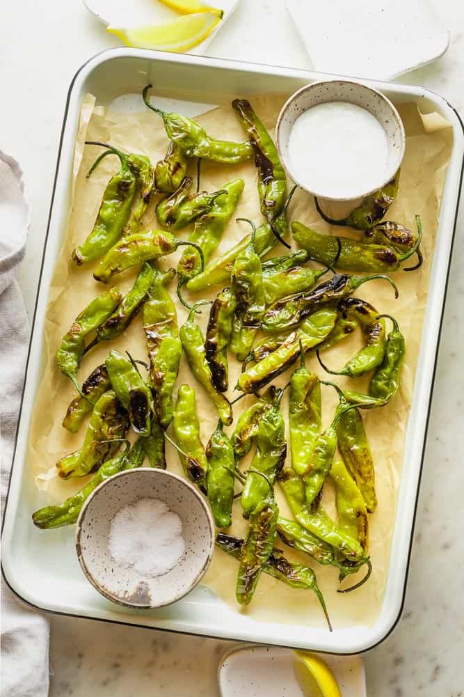 Blistered shishito peppers on a tray with yogurt garlic sauce