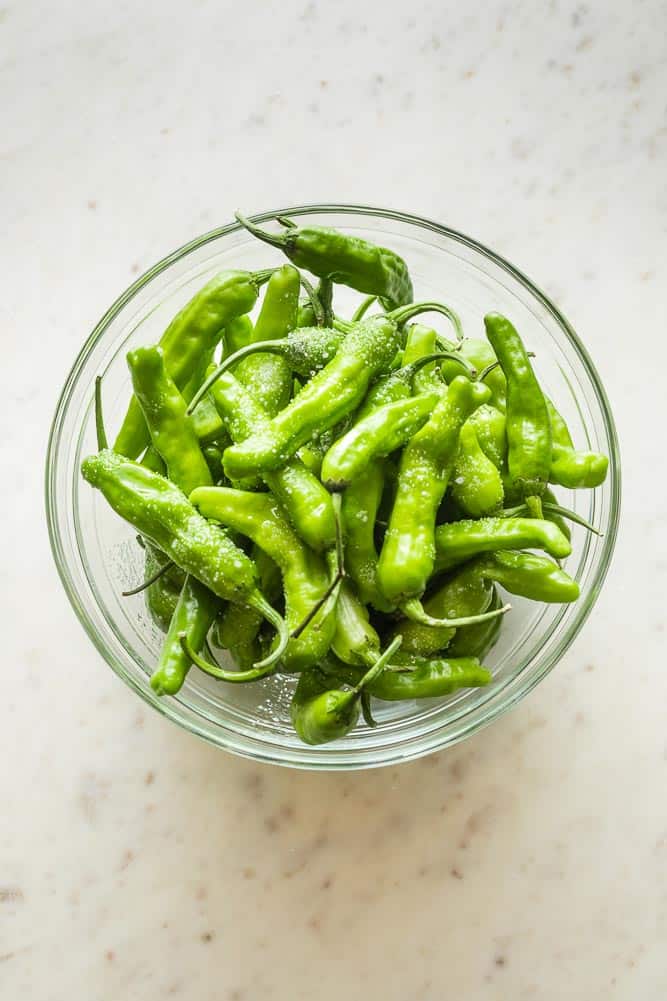 A clear glass bowl filled with shishito peppers