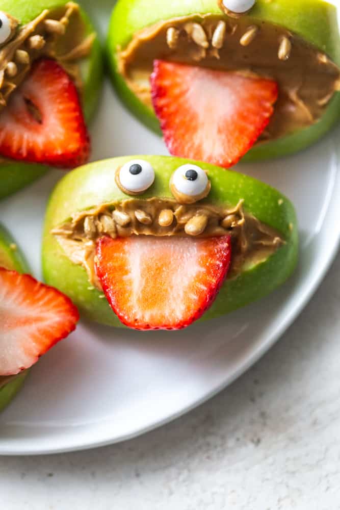 Apple monster treats made from a green apple, mouths cut out and filled with peanut butter, sunflower seeds for teeth and strawberry slices for tongues.  Candy eyes are attached at the top to make eyes for the "monster".