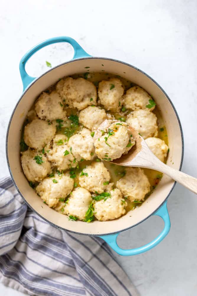 A Dutch oven of chicken and dumplings, with a spoon lifting one fluffy dumpling out of the pot.
