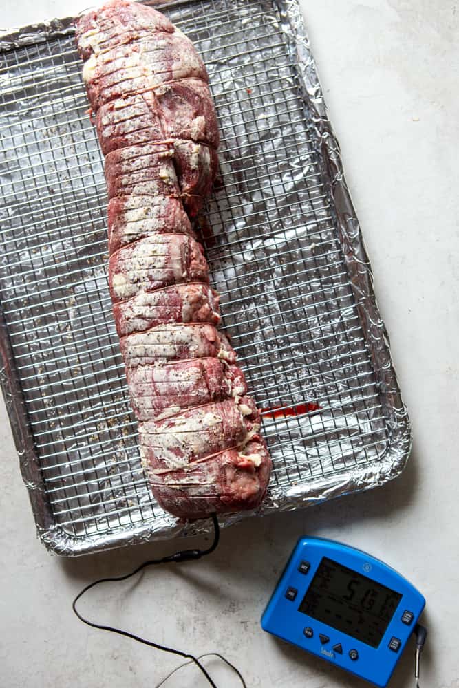 Uncooked beef tenderloin ties with kitchen twine and rubbed with butter, as well as ties with twine. Sitting on a cooling rack over a baking sheet that is lined with foil.