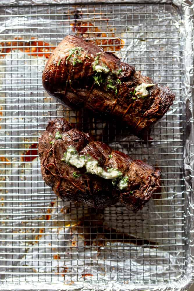 A cooked beef tenderloin that has been cut in half, topped with herb butter.