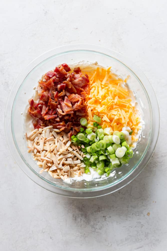 glass bowl with cream cheese mix topped with bacon, shredded cheese, green onions and slivered almonds.