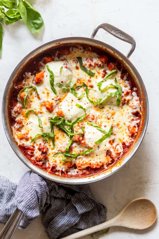 Cheesy One Pot Gnocchi with Sausage garnished with fresh basil on a large stainless steel skillet.