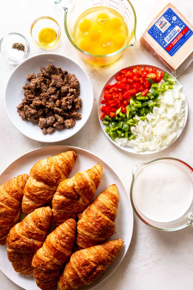Ingredients for overnight croissant breakfast Casserole - croissants, milk and cream, breakfast sausage, bell peppers, onions, eggs, gruyere cheese, salt, pepper and olive oil. 
