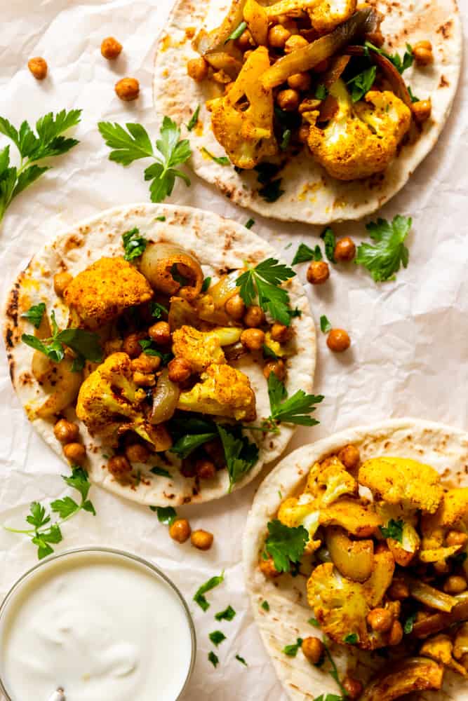 Pitas topped with roasted cauliflower and chickpeas, garnished with parsley.