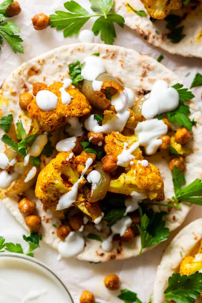 Roasted spiced Cauliflower and chickpeas on a pita, drizzled with garlic yogurt sauce and garnished with parsley. 