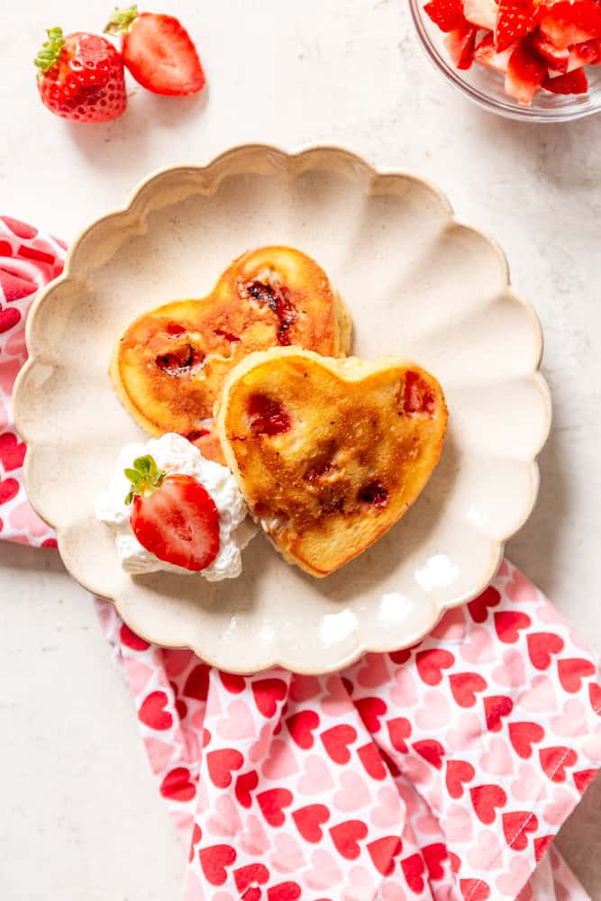 heart shaped strawberry pancakes on a scalloped plate with a heart napkin.
 
