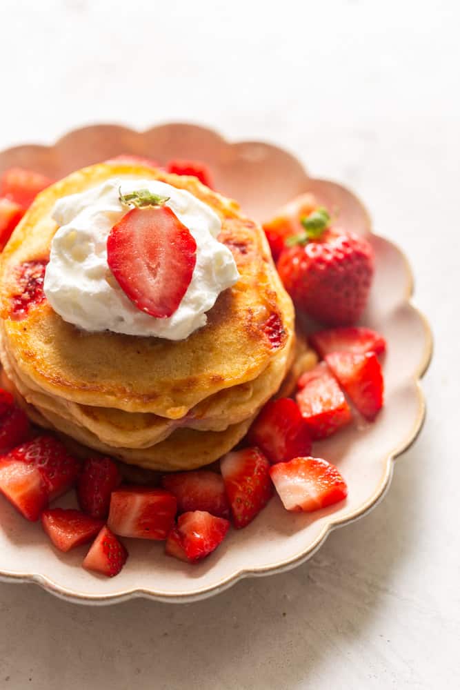 A stack of strawberry pancakes topped with whipped cream and a fresh strawberry.