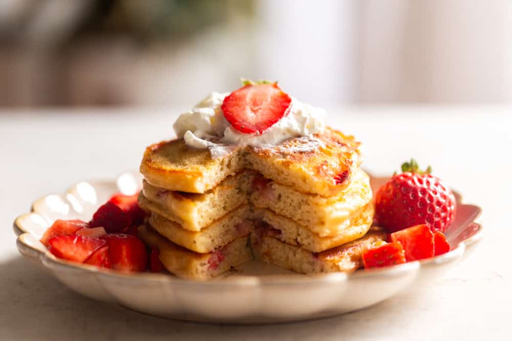 Strawberry pancakes after being cut, topped with whipped cream and strawberries.