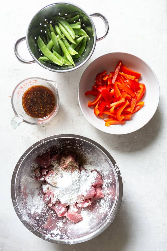 Ingredients for stir fry: Snap peas, sliced red bell pepper, stir fry sauce, pork cut into cubes in a bowl with cornstarch, salt and pepper.