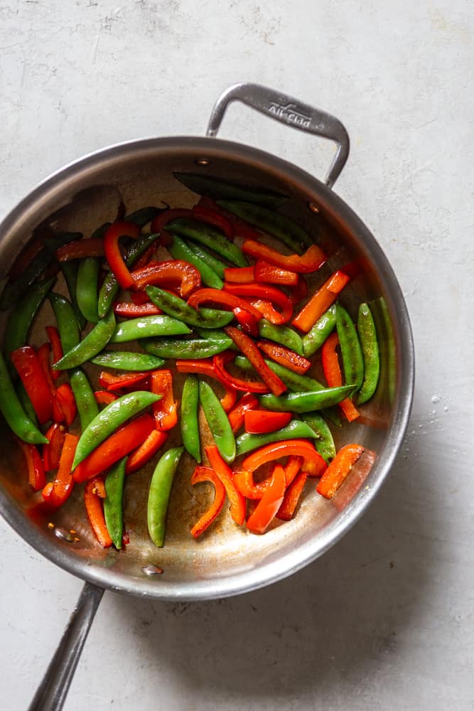 Snap peas and red bell peppers in a sautรฉ pan