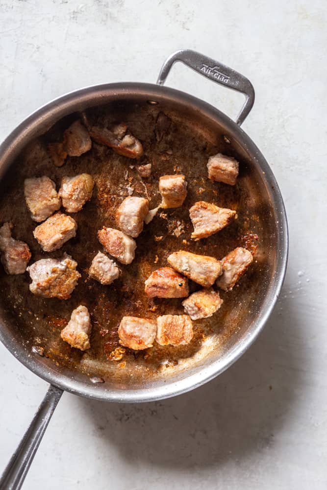 Pork being browned in a sautรฉ pan.