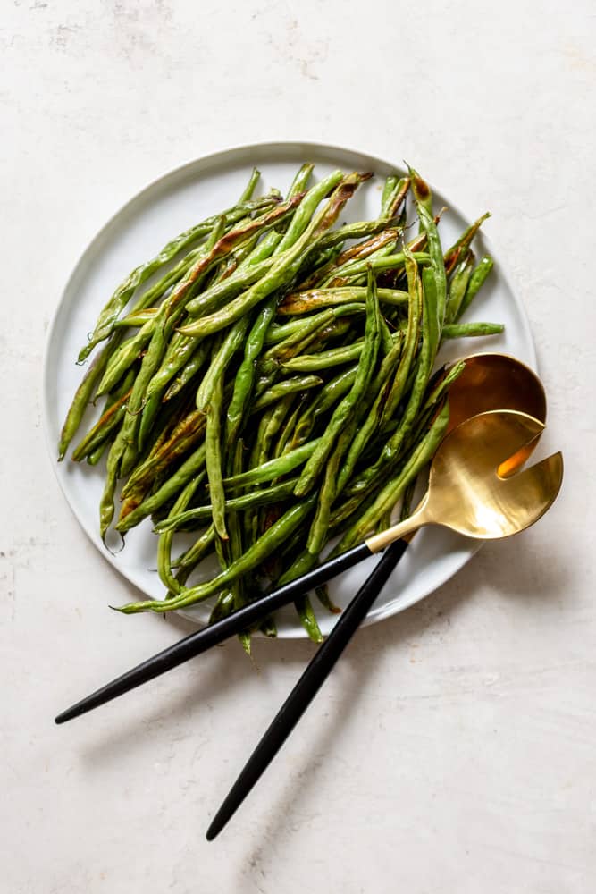 Oven Roasted Green Beans on a white plate with gold and black serving utensils.