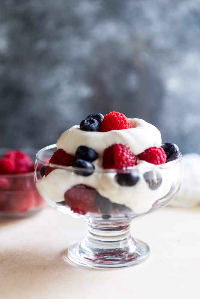 Homemade whipped cream with raspberries and blueberries in a glass dessert bowl. 