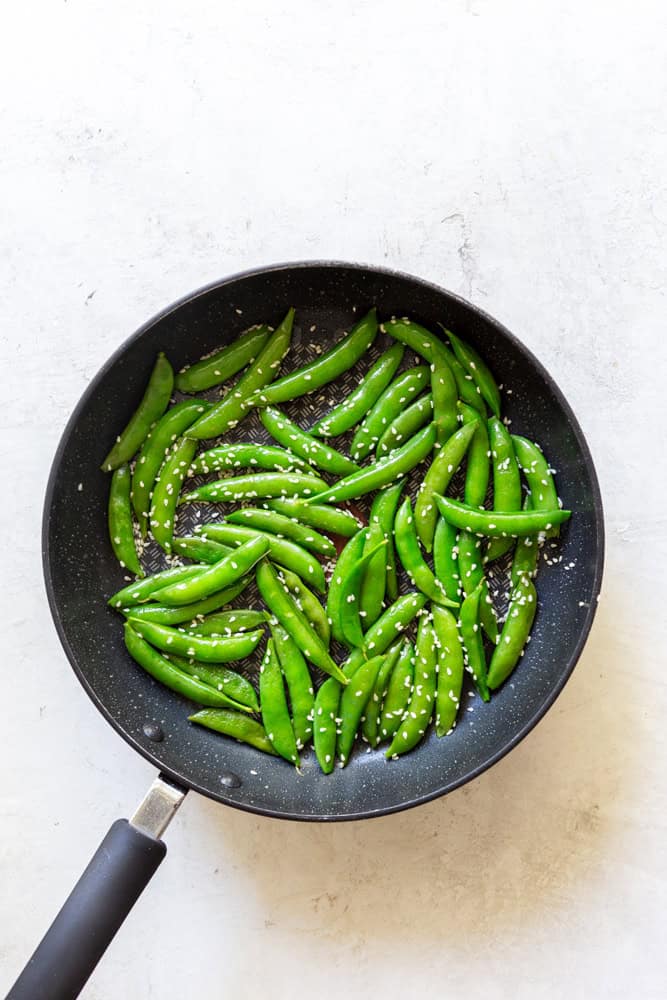 sesame snap peas in a pan with sesame seeds.