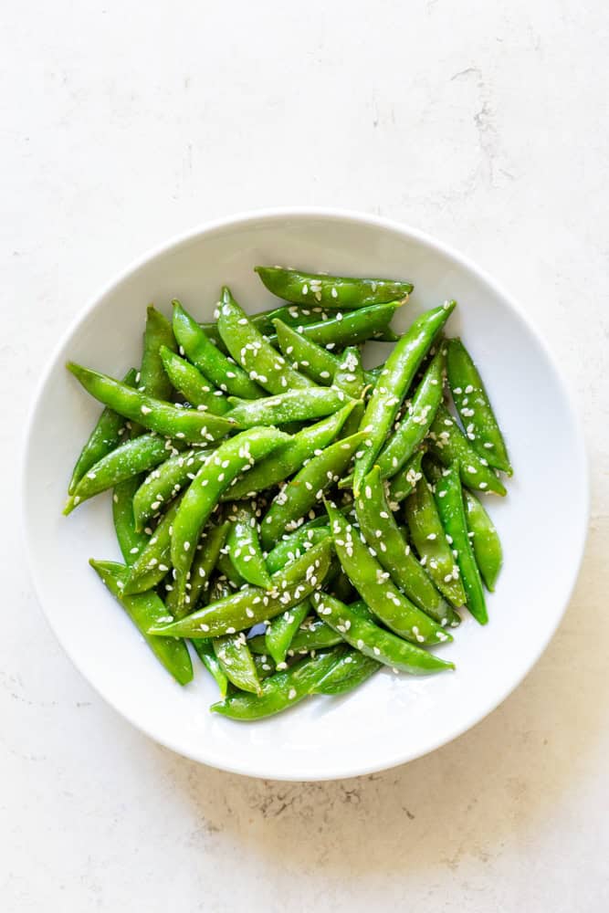 Sesame snap peas in a white bowl.