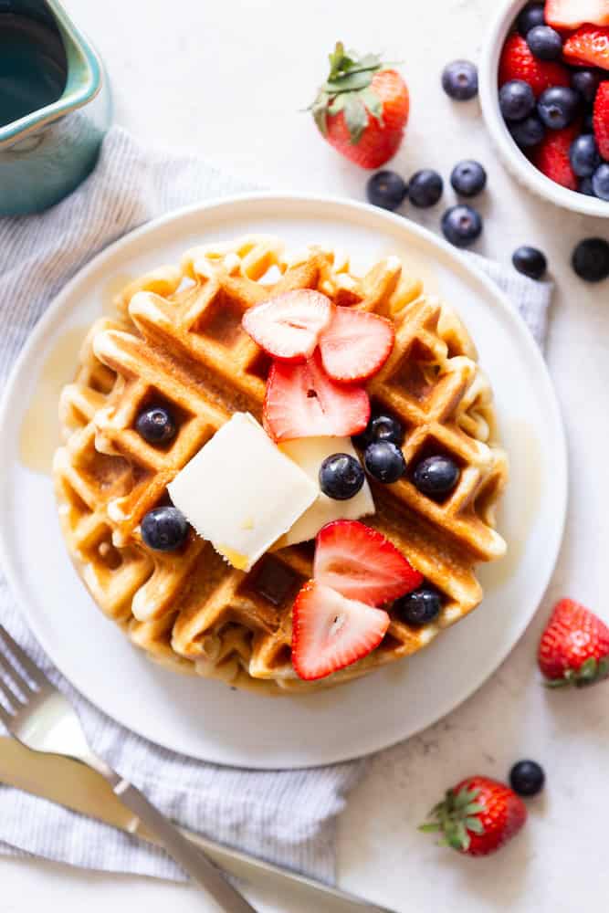 Buttermilk Waffle topped with sliced strawberries and blueberries, pats of butter and maple syrup.