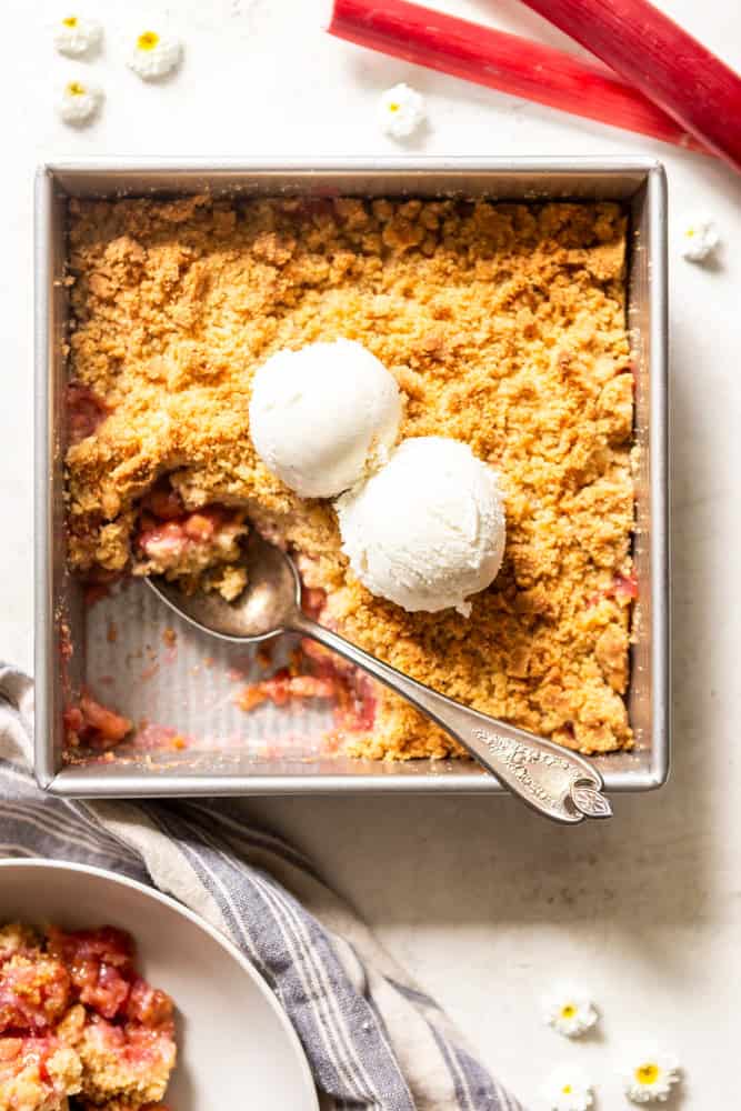 Square metal baking dish with baked rhubarb crumble, topped with vanilla ice cream.