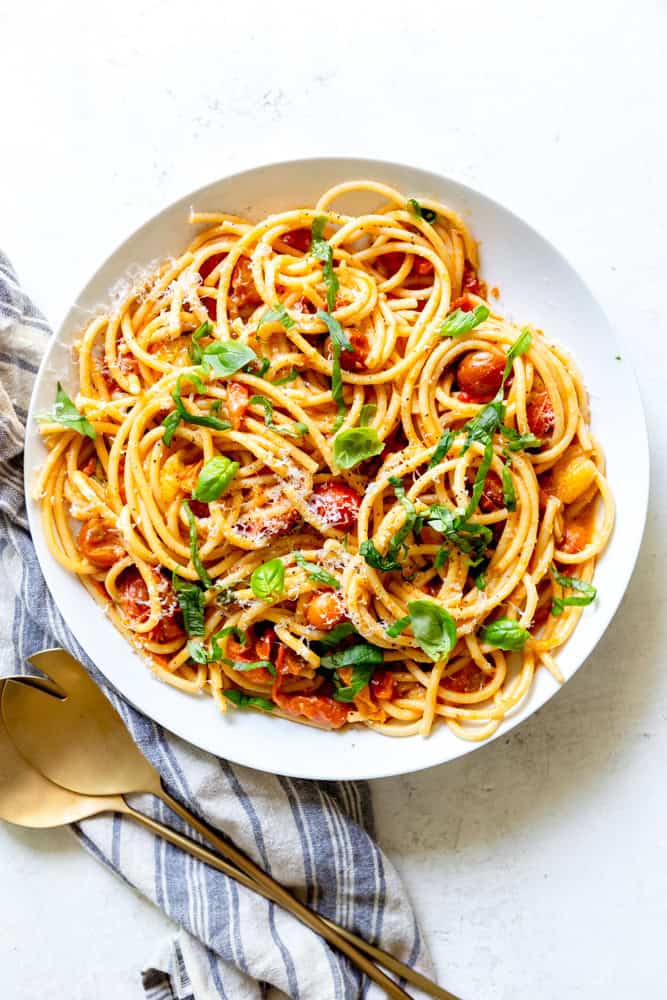 Burst Cherry Tomato Pasta garnished with basil and parmesan cheese, in a white serving bowl.