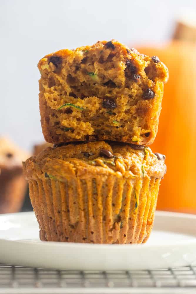 One half of a Healthy Pumpkin zucchini muffin stacked on top of a whole pumpkin zucchini muffin.