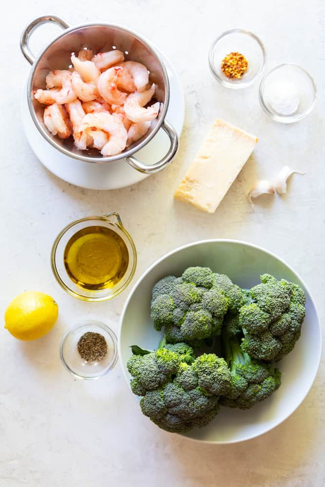 Ingredients for roasted shrimp and broccoli: Raw shrimp, red pepper flakes, salt, parmesan cheese, garlic, olive oil, broccoli, lemon, pepper.