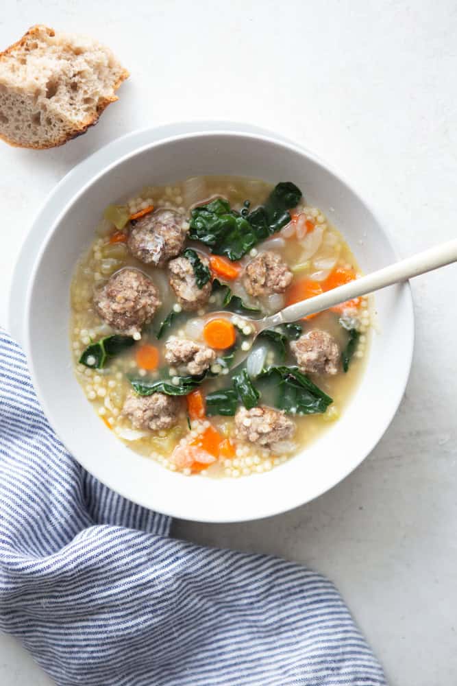 Italian wedding soup with mini meatballs and kale in a white bowl.