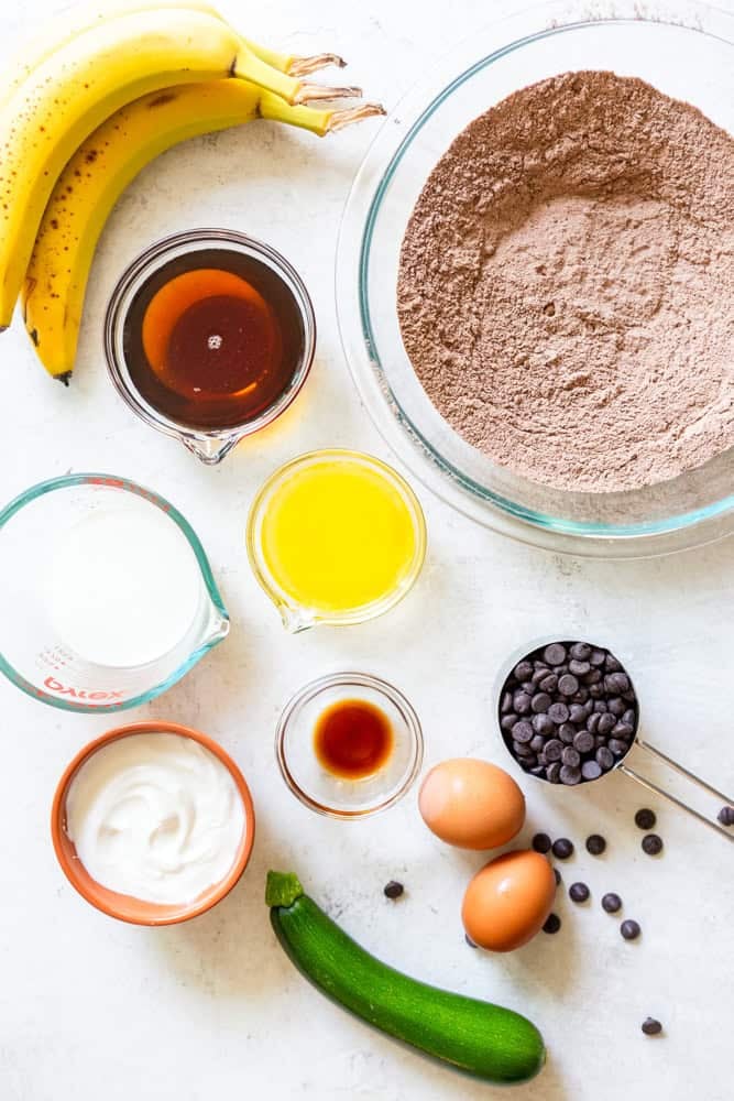 Ingredients for chocolate zucchini muffins - bananas, maple syrup, butter, milk, yogurt, vanilla, zucchini, eggs, chocolate chips, flour, cocoa powder, baking powder, baking soda, salt, cinnamon.