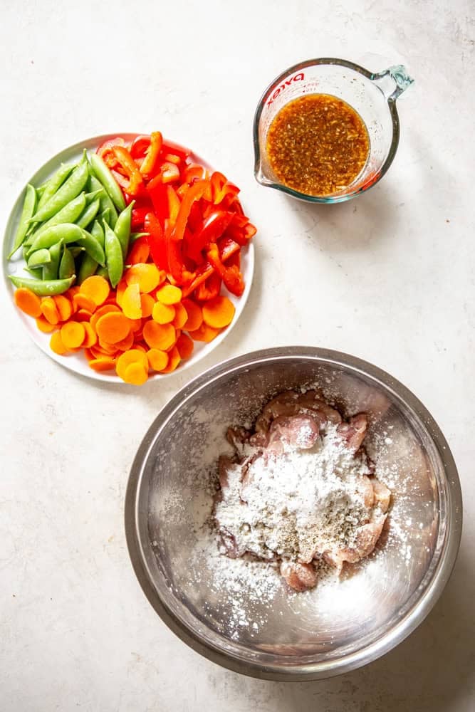 Ingredients for Honey Garlic Chicken Stir fry before cooking - honey garlic stir fry sauce, carrots, snap peas, red bell peppers, chicken thighs cut into 1 inch pieces with cornstarch, salt and pepper in a bowl.