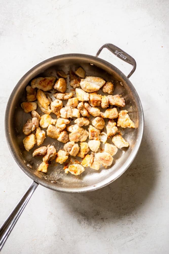 Chicken thigh pieces being cooked in a pan.