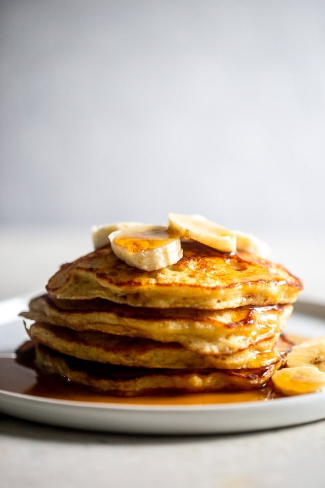 A stack of fluffy banana pancakes topped with bananas.
