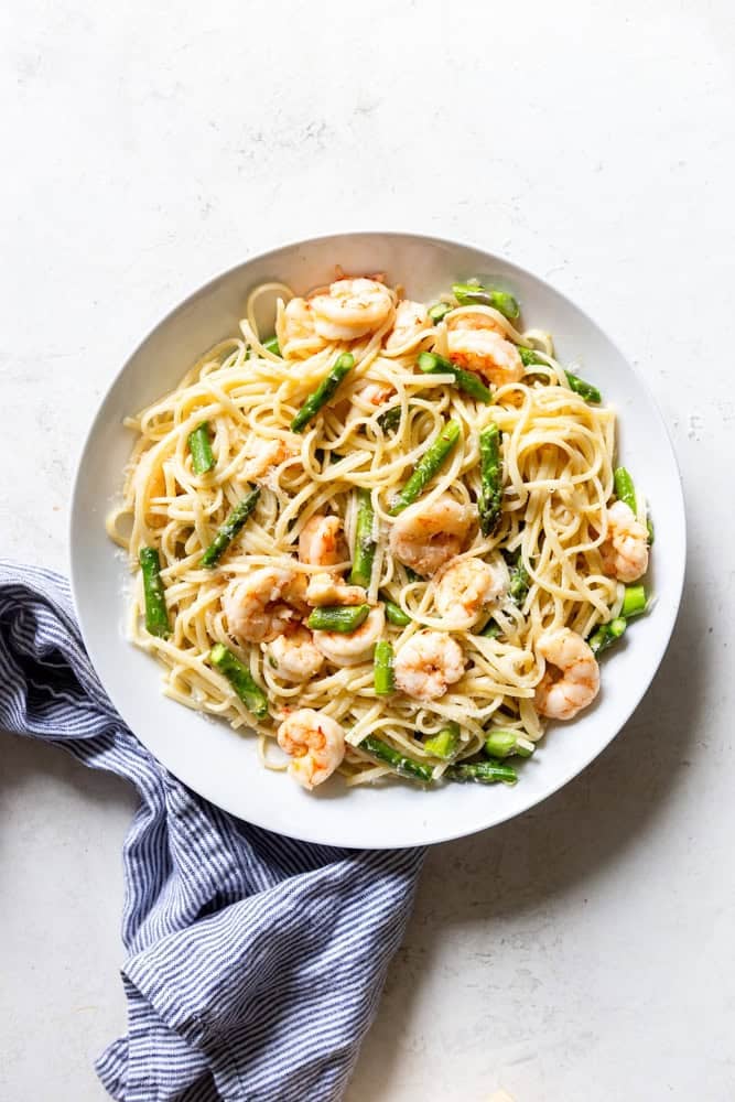 Pasta with shrimp and asparagus in a white bowl.